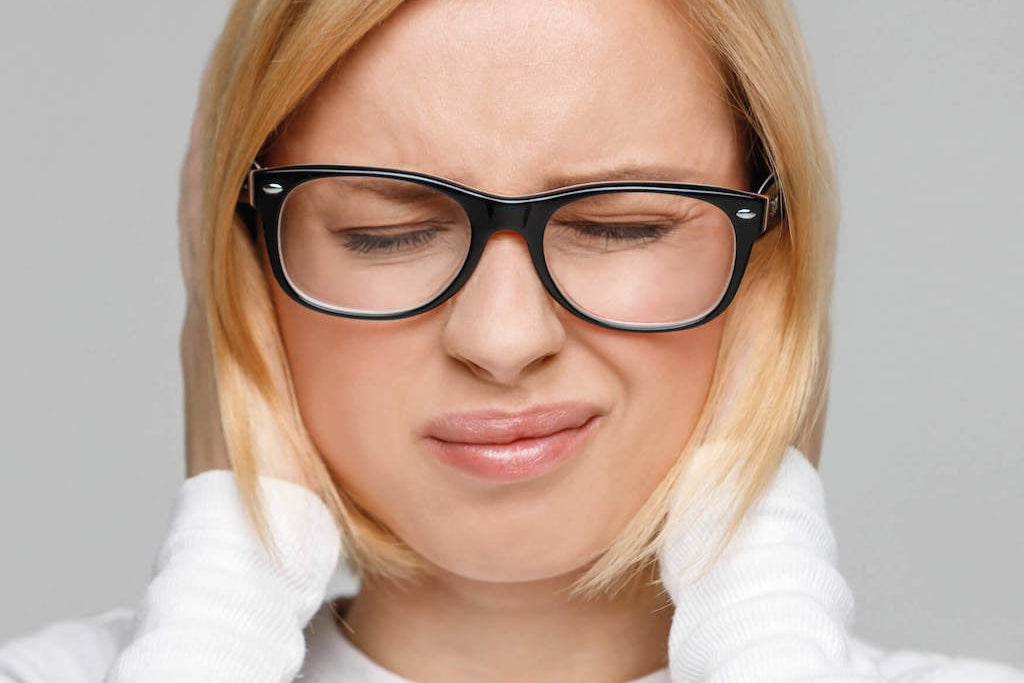 Darstellung einer Frau mit schmerzverzerrtem Gesicht, die sich die Ohren zu hält